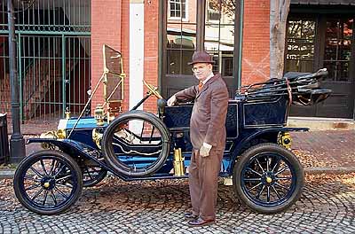 Photograph of Tony Cimorelli in front of Reggie Nash's 1911 Touring (Blue) on the movie set of Iron Jawed Angels filmed in Richmond Virginia during 2002.  Set is in Shockou Bottom.  Tony is in period costume of a brown suit and fedora hat.
